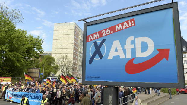 AfD supporters walking near a party elections poster in Erfurt, Germany. 