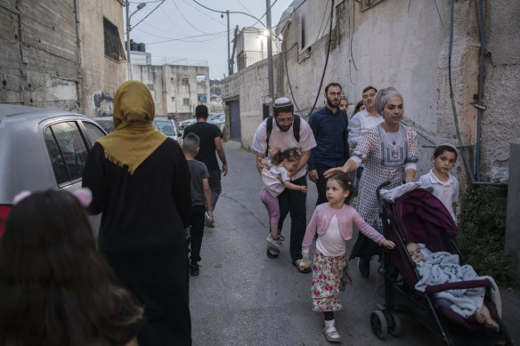 Israeli settlers walk past a Palestinian family in the Silwan district of East Jerusalem. Efforts to force Palestinians from Sheikh Jarrah set the stage for the recent Gaza war, and a similar dynamic looms here.