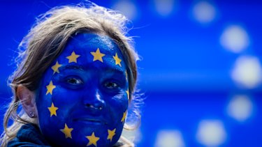 A woman wearing face paint in a European Union flag design follows the results of the European Parliament elections in Brussels.