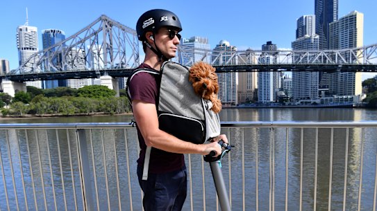 Michael Snowden and his pet cavoodle Snooks are seen riding his electric scooter along side the Brisbane River in Brisbane, Thursday, April 30, 2020. The Queensland Government has announced that some restrictions will be eased in Queensland due to a very low number of new COVID-19 infections from Saturday, May 2. Queenslanders will be able to go for a drive (within 50km of home), ride a motorbike, jetski or boat for recreation, have a picnic, visit a national park and shop for non-essential items. (AAP Image/Darren England) 