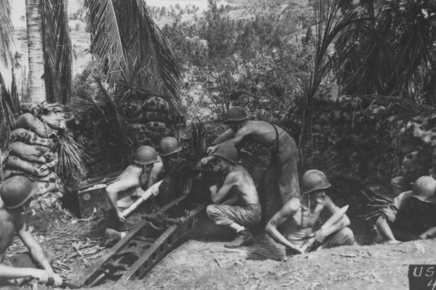 Camouflaged by the jungle and protected by sand bags, a Marine crew loads ammunition in the Solomon Islands, 1942.