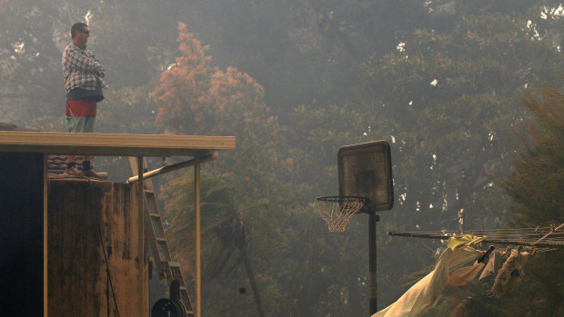 A man stands on the roof of his house as an out of control bushfire approaches, on Lemon Tree Passage road in Salt Ash.