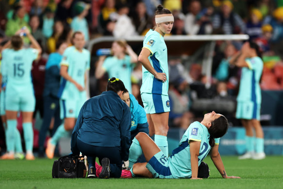 Sam Kerr is attended to by medical staff as a bandaged Caitlin Foord watches on.