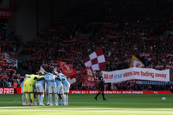 Manchester City huddles before the match, with banners in the background alluding to the cheating scandal.