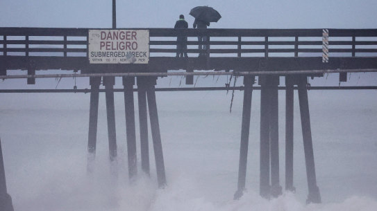 People in California stand on a pier over the Pacific Ocean with Hurricane Hilary approaching.