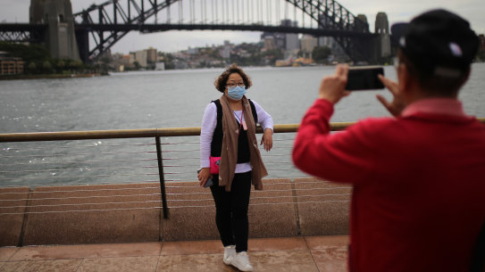 People wearing face masks as a preventative measure against coronavirus COVID-19 take photos in front of the Sydney Harbour Bridge in Sydney.