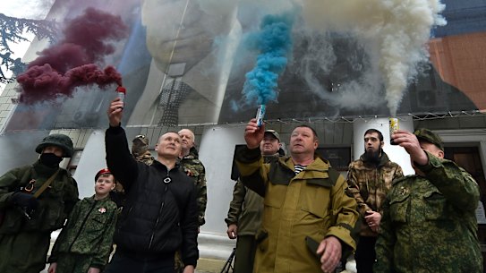 People hold flares in colours of the Russian national flag during an action to mark the ninth anniversary of the Crimea annexation from Ukraine with an image of Russian President Vladimir Putin.