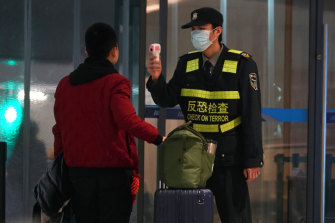 An airport staff member uses a temperature gun to check people leaving Wuhan Tianhe International Airport.