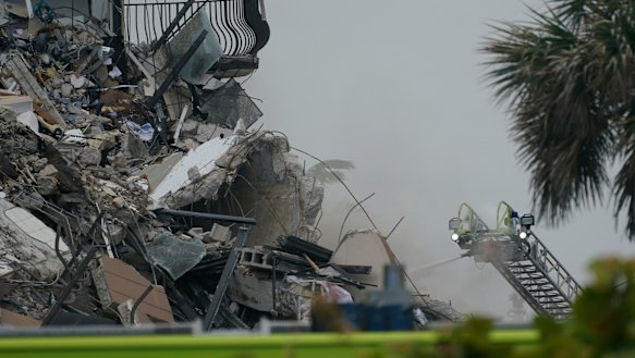 Firefighters use a ladder hose as smoke comes out of the rubble of the partially collapsed building.