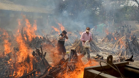 Relatives react to heat emitting from the multiple funeral pyres of COVID-19 victims at a crematorium in the outskirts of Delhi, India. 