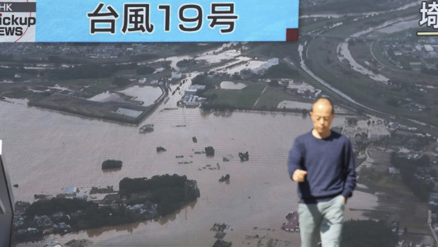 A man walks in front of huge TV screen showing a news program with footage of one of areas devastated by Typhoon Hagibis.