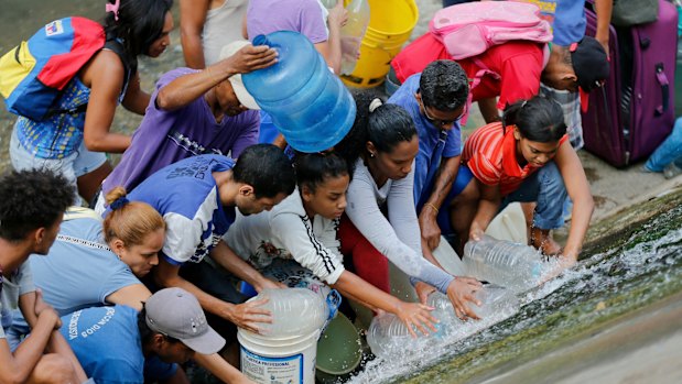 People collect water falling from a leaking pipeline along the bank of the Guaire River during rolling blackouts, which affects the water pumps.