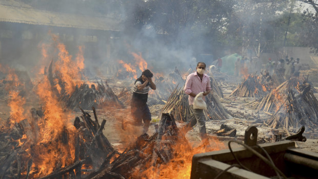 Relatives react to heat emitting from the multiple funeral pyres of COVID-19 victims at a crematorium in the outskirts of Delhi, India. 