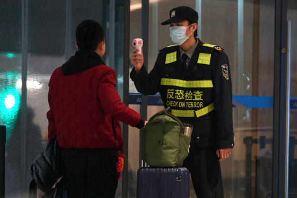 An airport staff member uses a temperature gun to check people leaving Wuhan Tianhe International Airport.