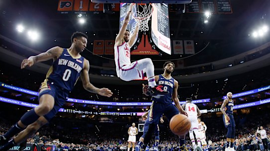 Ben Simmons hangs from the rim after a dunk past New Orleans Pelicans' Nickeil Alexander-Walker and Jahlil Okafor. 