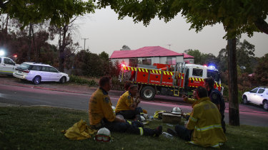 Firefighters take a break near properties where fire retardant was dropped on Barwon Avenue during a fire in South Turramurra.