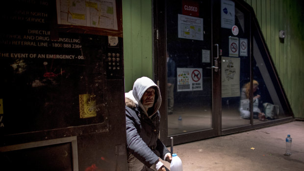 A man sits next to the needle vending machine outside the safe injecting room.
