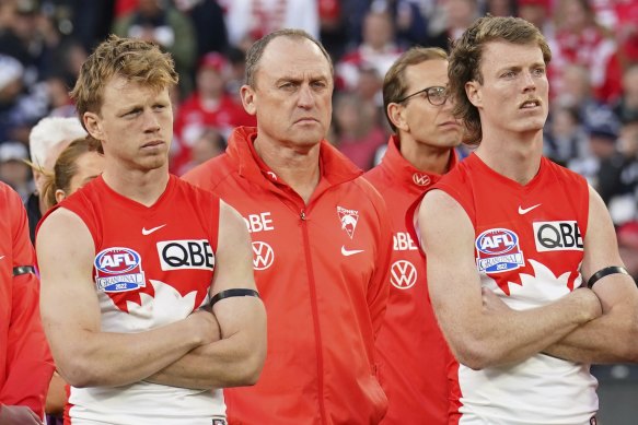 Callum Mills, John Longmire and Nick Blakey look on as Geelong players collect their premiership medals.