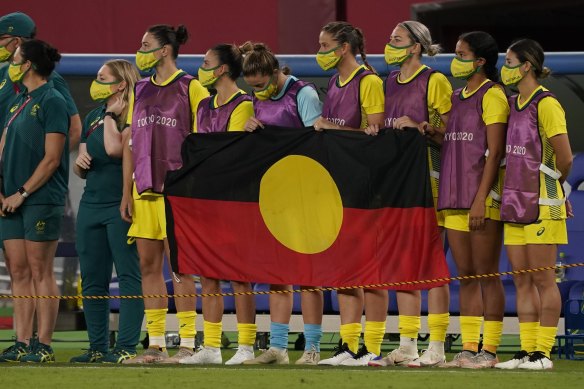 The Matildas line up behind the Aboriginal flag at the Tokyo Olympics.