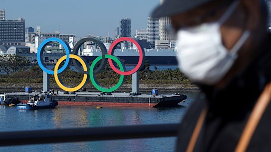 A man wearing a protective face mask to help curb the spread of the coronavirus walks with the Olympic rings in the background in Odaiba. 