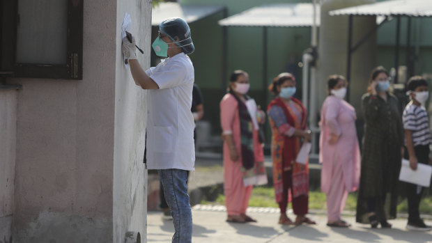 A doctor fills a form, as others wait in a queue for COVID-19 tests in Jammu, India this week. 