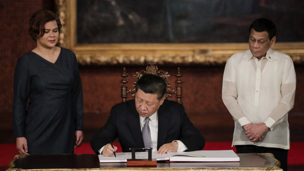 Chinese President Xi Jinping signs the guest book as Philippine President Rodrigo Duterte and daughter Sara Duterte look on last year.