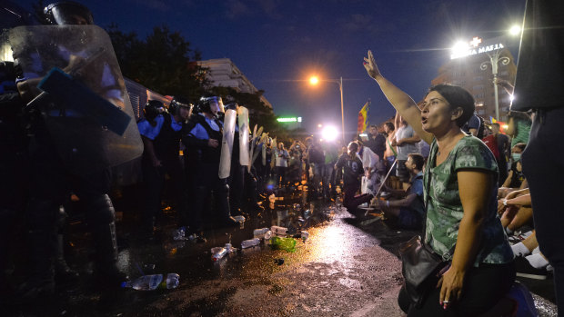 A woman shouts slogans in front of a riot police line during protests outside the government headquarters, in Bucharest, Romania.