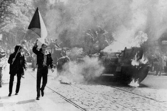 Defiant young Czechs carrying their country's flag past a burning Soviet tank on a street in Prague.