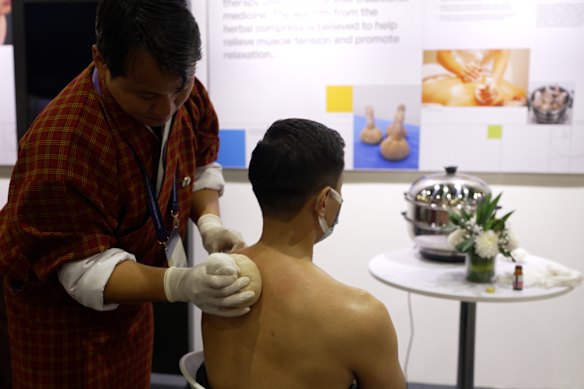 A Bhutanese traditional practitioner applies a hot herbal compress to a conference delegate.
