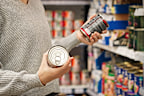 Stock image of a woman holding tins in the supermarket aisle.