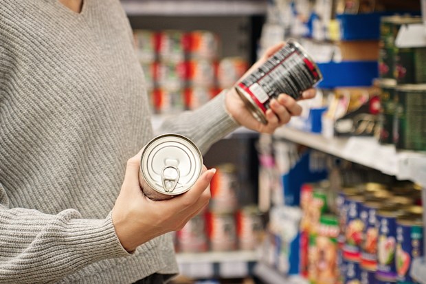 Stock image of a woman holding tins in the supermarket aisle.