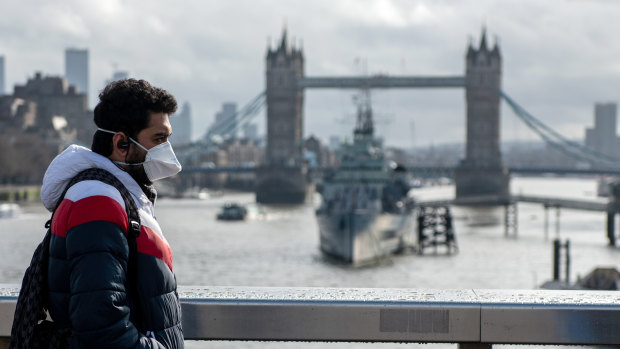 A man wearing a mask walks over London Bridge in central London with the Tower Bridge behind.