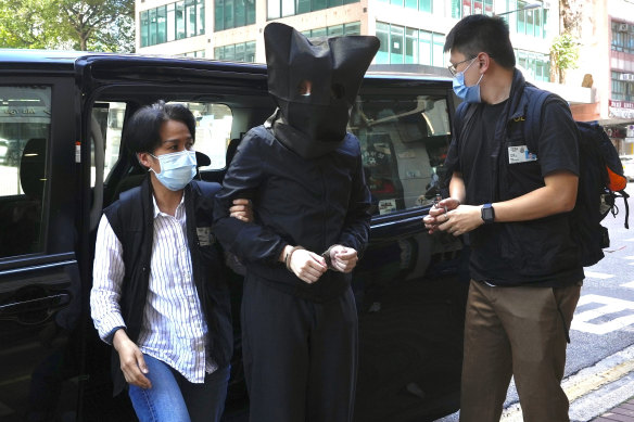 A hooded suspect is accompanied by police officers to search evidence at office in Hong Kong in July 2021 during the investigation of the case.