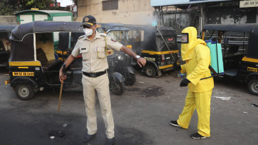 A civic worker sprays disinfectant on a policeman standing guard after a protest by migrant workers against the extension of the lockdown, in a slum in Mumbai.