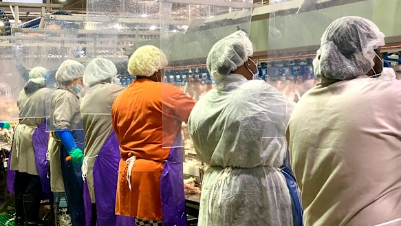 Tyson Foods workers in Georgia wear protective masks and stand between plastic dividers. The company is now mandating vaccinations.