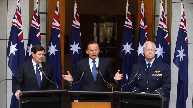 Then-prime minister Tony Abbott in 2015 announcing preparation for a troop deployment to Iraq. He is joined by then-Defence Minister Kevin Andrews and former Defence Force chief Air Chief Marshal Mark Binskin, and a number of national flags.