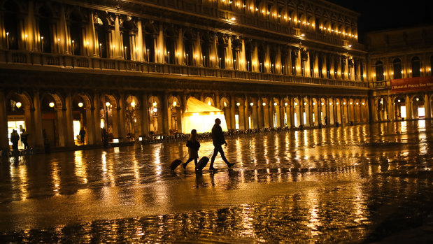 Tourists pull their trolleys as they walk through a nearly empty St Mark's Square on a rainy day in Venice.