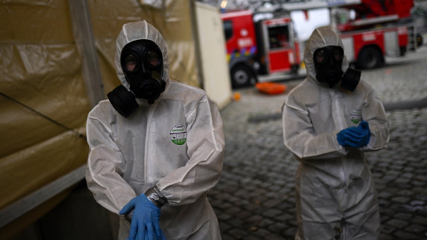 Military personnel, wearing full protective equipment, clean their hands after disinfecting an ambulance used to carry a coronavirus COVID-19 patient in Brussels.
