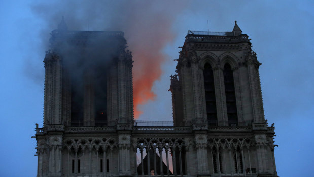 Smoke and flames fill the sky as a fire burns at the Notre-Dame Cathedral during a visit by French President Emmanuel Macron in Paris.