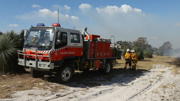 Firefighters watch over burnt bushland and scrub behind homes that run along the Tilligerry Track, Tanilba Bay.