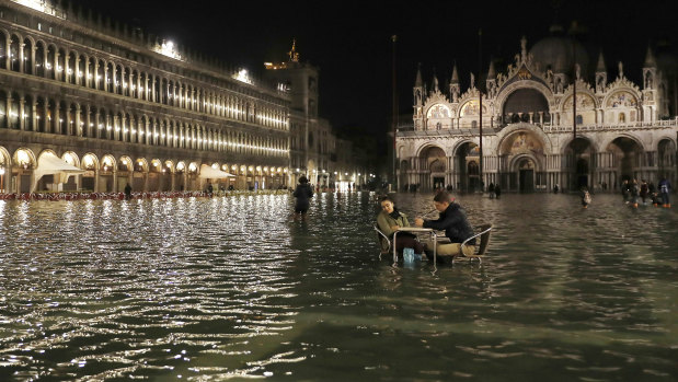 Rising seas: People sit in a flooded St Mark's Square in Venice, Italy, as high tides inundated the city in March 2018.