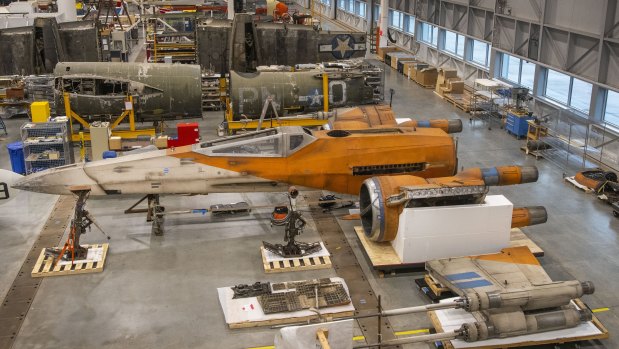 A Star Wars X-wing fighter is being constructed and conserved next to a World War II-era air plane in the Smithsonian’s restoration hangar. 