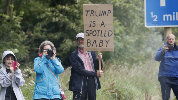 People hold posters when watching the motorcade vehicles transporting Donald Trump and First Lady Melania Trump, on the road leaving Trump Turnberry golf resort, Scotland.