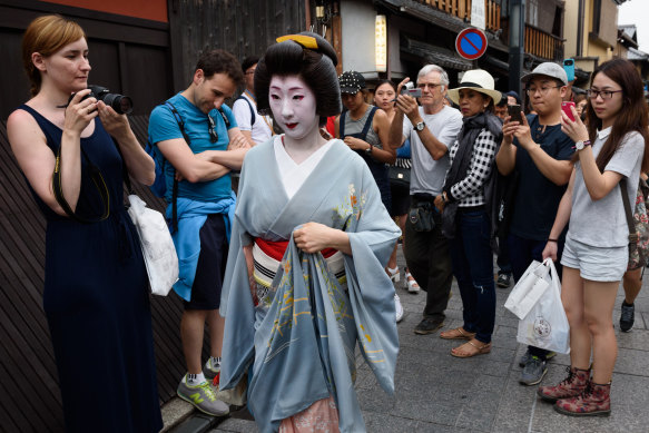Tourists photograph a geiko walking through Gion in Kyoto.