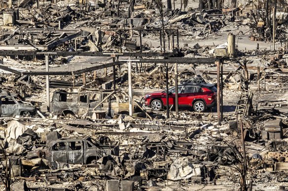 A car drives past homes and vehicles destroyed by the Palisades fire at the Pacific Palisades Bowl Mobile Estates.