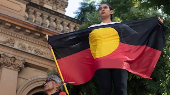 A protester holds an Aboriginal flag at a rally to mark 30 years since the royal commission. into deaths in custody.