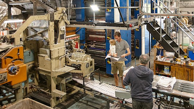 Michael Waite (holding daughter Hazel) examines an issue of his fledgling newspaper as it comes off the printing press. The paper’s motto is “locals helping locals”.
