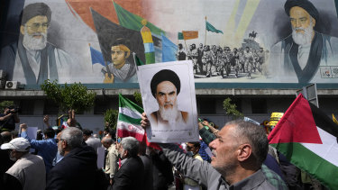 People walk past a mural showing Ayatollah Khomeini, right, Supreme Leader Ayatollah Ali Khamenei, left, while holding a poster of Ayatollah Khomeini and Iranian and Palestinian flags in an anti-Israeli march after Friday prayers in Tehran.