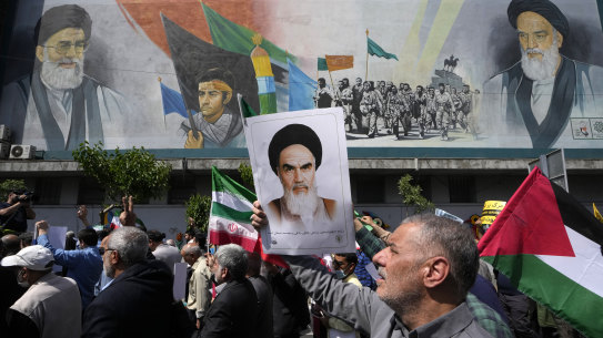 People walk past a mural showing Ayatollah Khomeini, right, Supreme Leader Ayatollah Ali Khamenei, left, while holding a poster of Ayatollah Khomeini and Iranian and Palestinian flags in an anti-Israeli march after Friday prayers in Tehran.