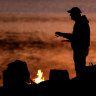 FILE IMAGE: A man warms himself next to a campfire at dusk.